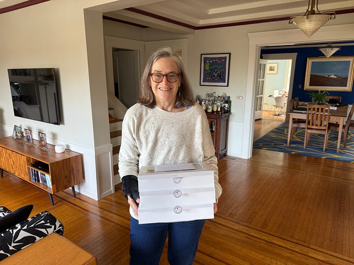 One image ofnthe author holding three white cardboard boxes of cookies, and another i age showing the cookies through clear lids