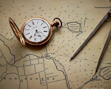 An antique pocket watch rests alongside a pair of navigational dividers on a vintage map, highlighting Sheep Porcupine Island near Bar Harbor.