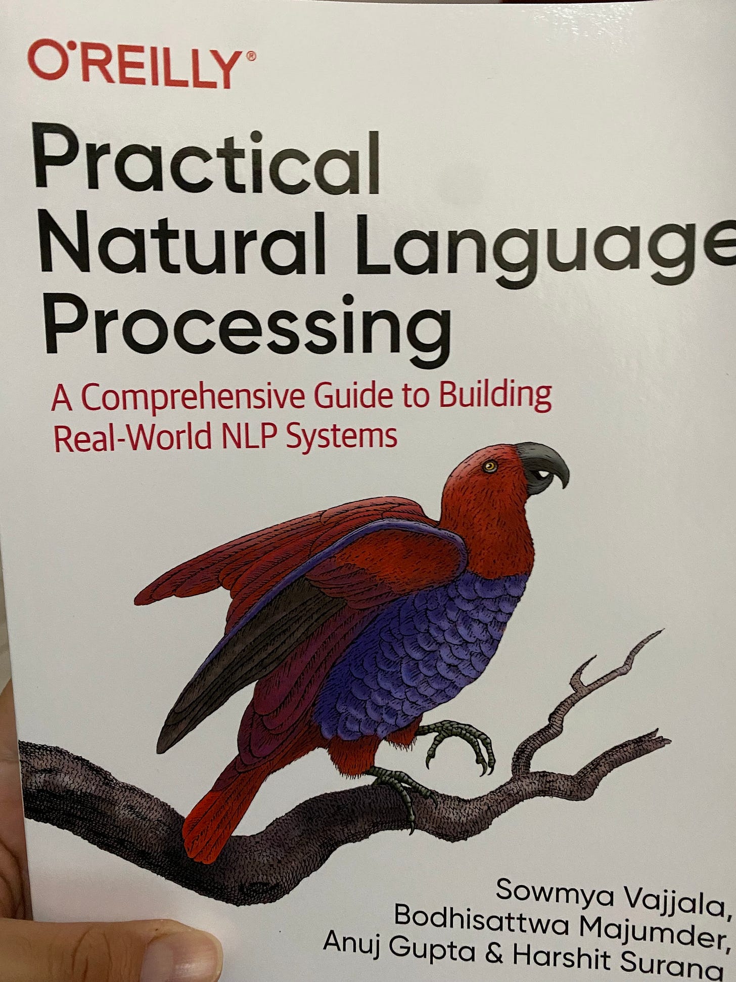 Portada de un libro llamado en inglés: Practical Natural Language Processing que contiene un ave de plumas rojas con pecho azul-púrpura parado sobre en un pie en un rama de árbol sin hojas