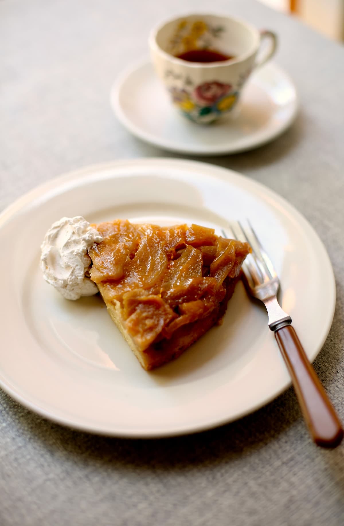 a piece of apple cake and a cup of tea on a table with a white plate and fork.