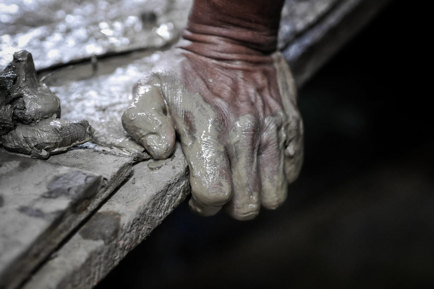 A  hand covered in grey wet cement, obviously straining to  support weight with sinew and tendon and veins flexing
