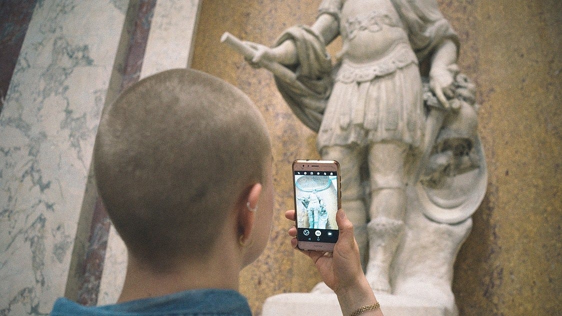 A person, shown from behind, is taking a picture of a sculpture with their smartphone. A person, shown from behind, is taking a picture of a sculpture with their smartphone.