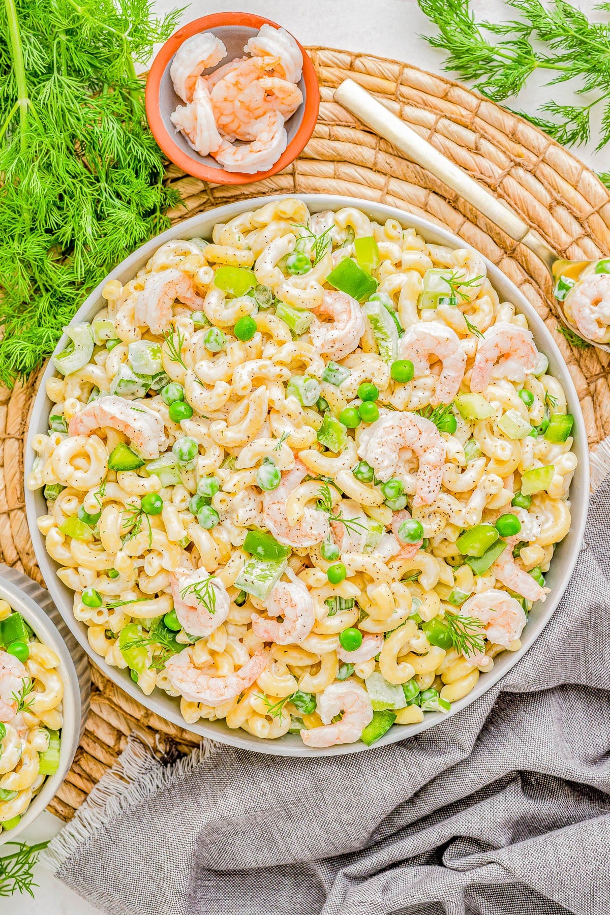 A vibrant shrimp pasta salad with green peas, dill, and cashews, served on a white platter over a rustic wicker mat and grey linen. A vibrant shrimp pasta salad with green peas, dill, and cashews, served on a white platter over a rustic wicker mat and grey linen.