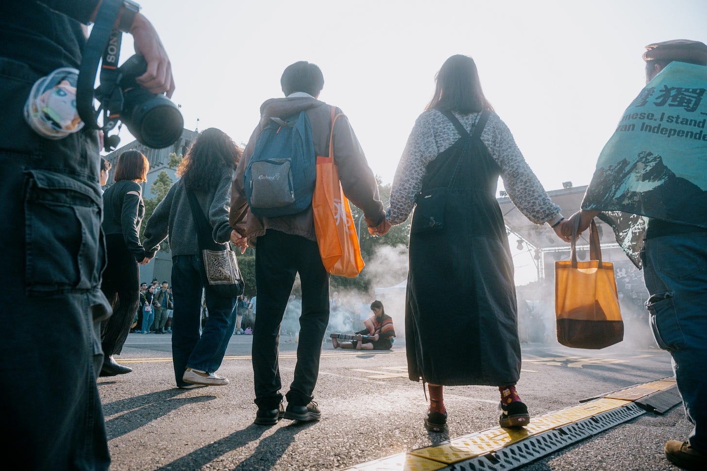 People standing, hand holding hands in a ring around a person performing a smoke ceremony in the middle of the ring. Other onlookers are in the background. (Image contributed by Philip So)