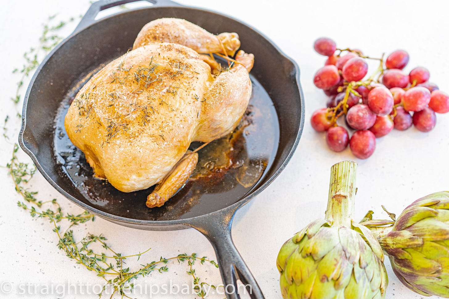 Whole roasted chicken with fresh thyme in a cast iron skillet, golden brown crispy skin
