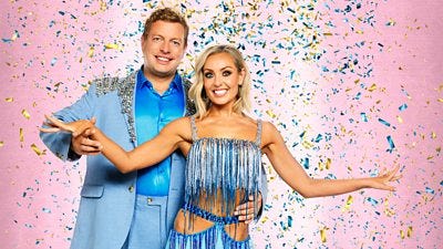 Thomas wears a blue slik shirt beneath a light blue suit, trimmed with sparkles. Amy wears a blue and silver fringe trimmed top and skirt with cutout detail.