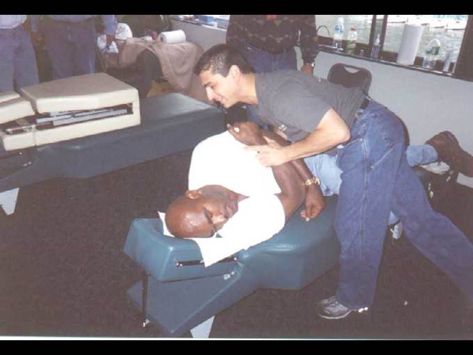 Chiropractor adjusts the back of a man in a white shirt lying face down on a chiropractic table