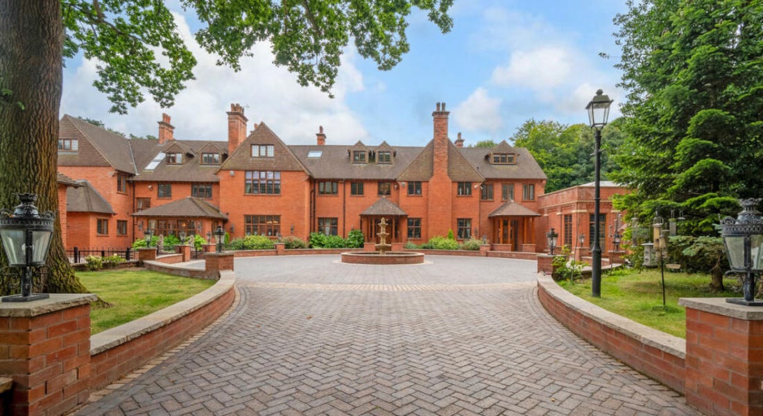 A large red brick country home with a brown roof, and a driveway with stone tiles and a roundabout