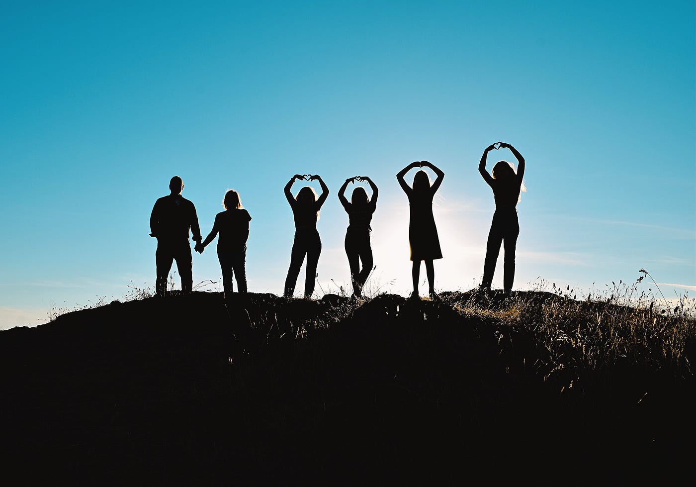 A family of six, two parents holding hands, four daughters are making hearts with their fingers, backlit by the sun. A family of six, two parents holding hands, four daughters are making hearts with their fingers, backlit by the sun.