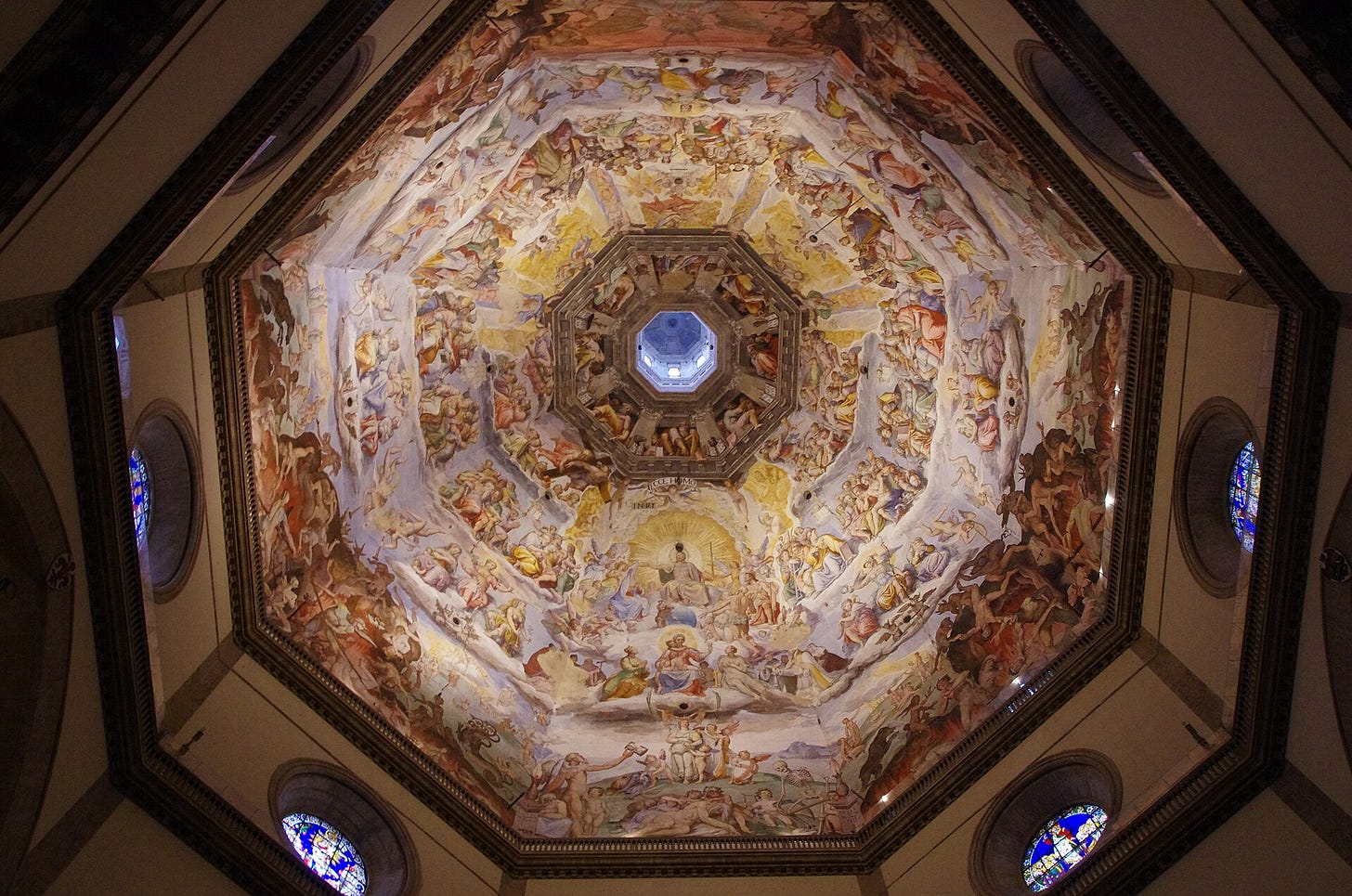 View straight up into an octagonal dome covered in painted rings of figures on clouds, with Christ in a pale circle on the lower edge of the picture and a small round window of light at the very top.