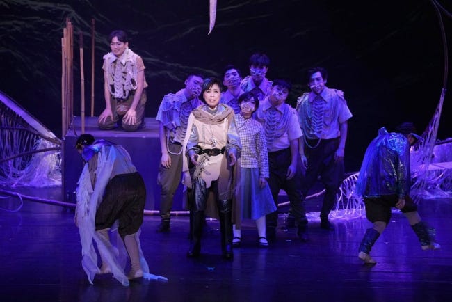 Image de l'opéra réprésentant une jeune femme sur scène en costume militaire du futur, cape et cuissardes blanches, entourée de danseurs Image de l'opéra réprésentant une jeune femme sur scène en costume militaire du futur, cape et cuissardes blanches, entourée de danseurs