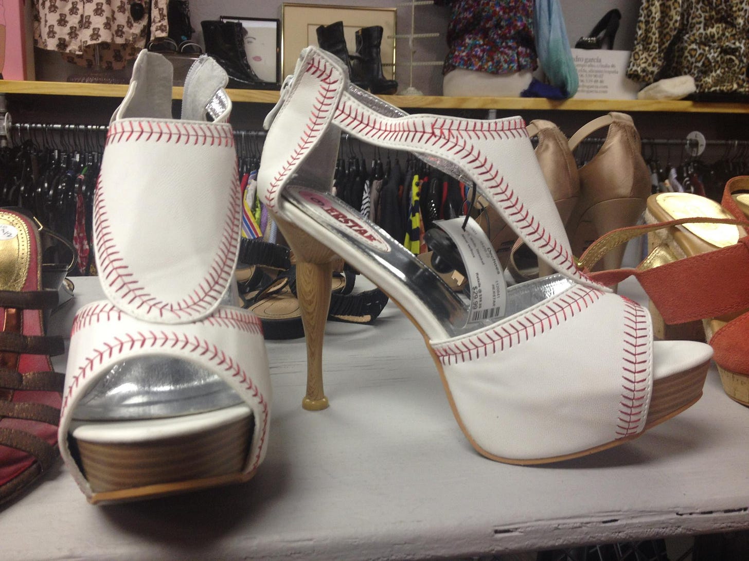 a pair of high heeled women's shoes made from white leather with red stitching, like baseballs, with little baseball bats for the spike heels. a pair of high heeled women's shoes made from white leather with red stitching, like baseballs, with little baseball bats for the spike heels.