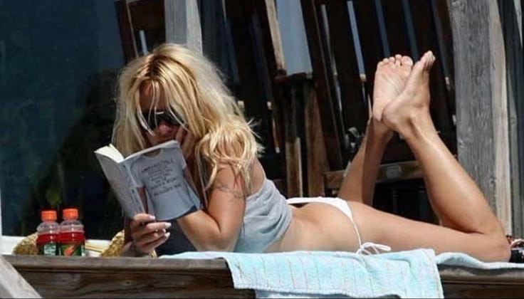 This may contain: a woman laying on the beach reading a book