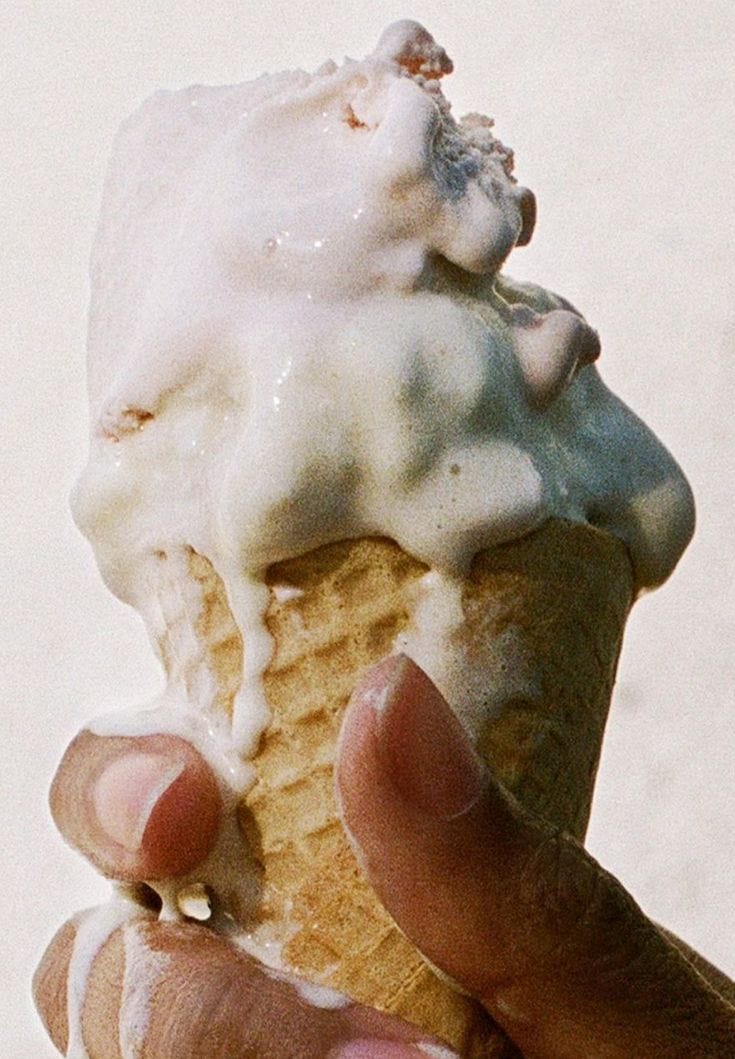 This may contain: a hand holding an ice cream cone with icing on it This may contain: a hand holding an ice cream cone with icing on it