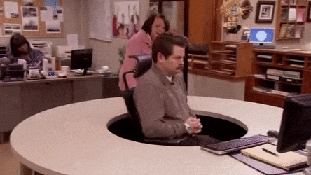 Office scene where a man sits sunken into a hole in a round desk, with a coworker walking past Office scene where a man sits sunken into a hole in a round desk, with a coworker walking past