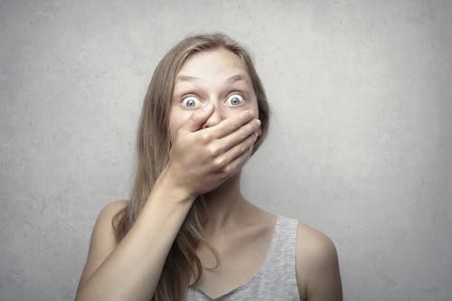 Free A startled woman covers her mouth expressing surprise against a neutral background. Stock Photo