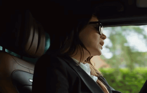 a woman wearing sunglasses and a suit is driving a car