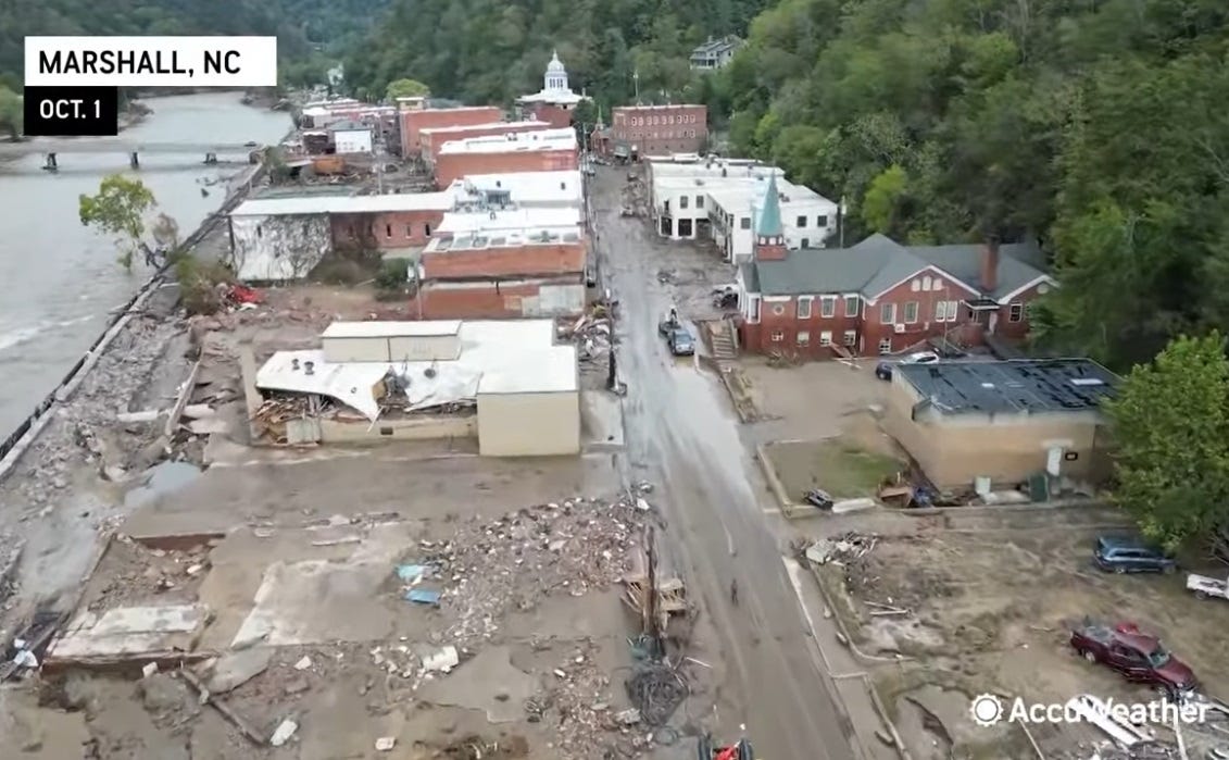 drone camera view of storm damage, partly wrecked buildings, muddy roads, empty foundations where buildings stood.