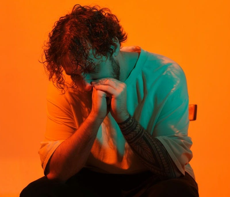 a man sitting on top of a chair in front of an orange wall a man sitting on top of a chair in front of an orange wall