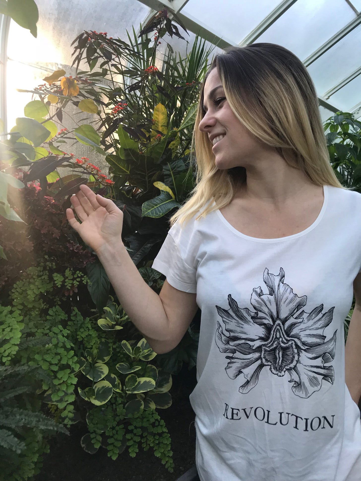 A woman wearing a floral t-shirt beside a large stand of plants.