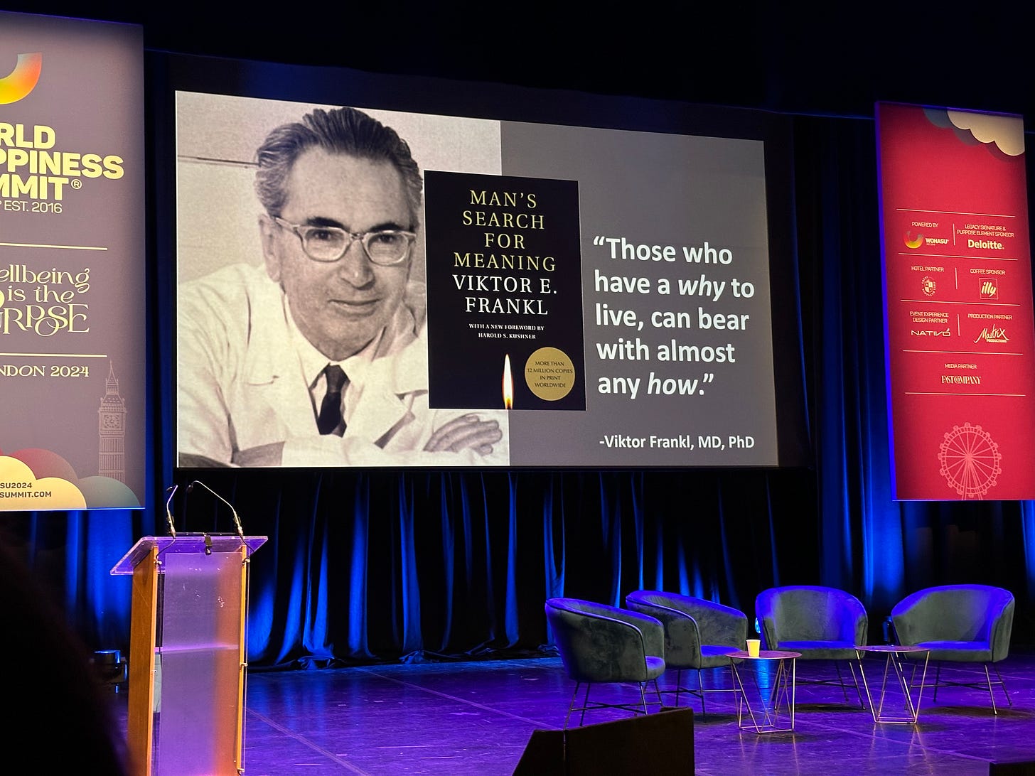 A photograph of the stage at WOHASU with a screen featuring Dr Kelli Harding's presentation. The slide has a photo of Viktor Frankl and his book 'Man's Search for Meaning' along with the quote "Those who have a why to live, can bear with almost any how."