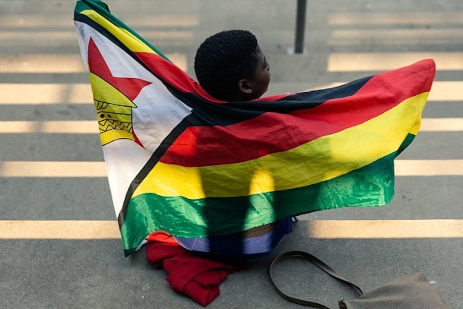 A child draped in Zimbabwe's national flag sits on the ground with her back to the camera. A child draped in Zimbabwe's national flag sits on the ground with her back to the camera.