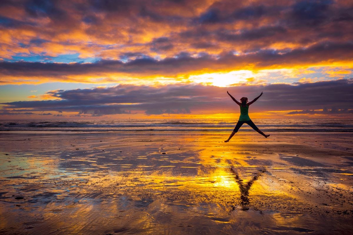 Woman doing hero jump on beach at colorful sunset