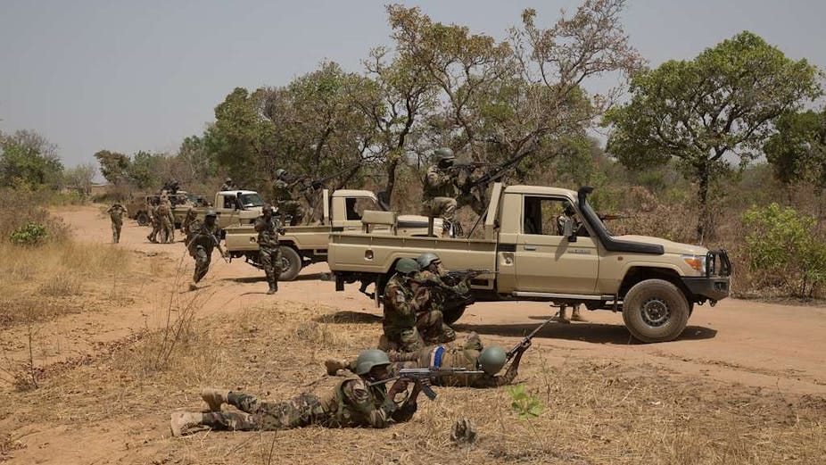 Vehicles parked on an unpaved roads, with soldiers in uniform in and around them