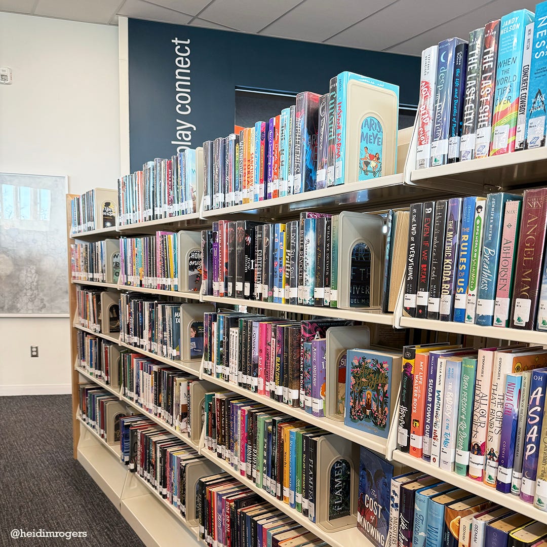 Library bookshelf, filled with young adult titles. In the background is a white wall and a blue wall, that reads "play connect."