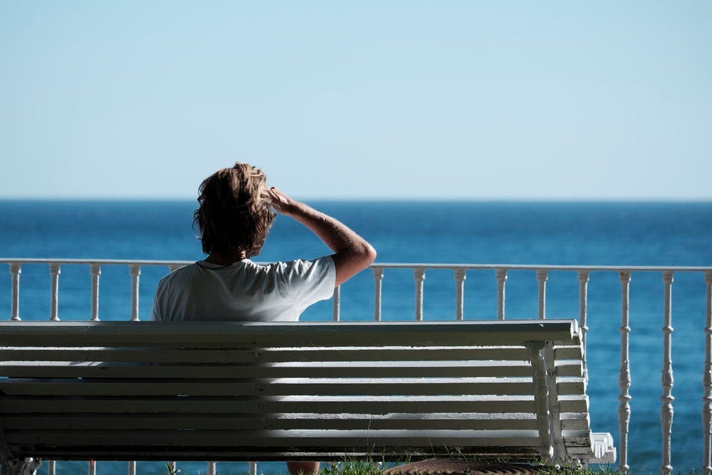 man sitting on bench near body of water during daytime man sitting on bench near body of water during daytime