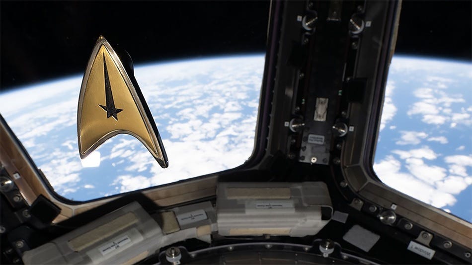 photo of a star trek badge floating in the air with the windows of the Space Station behind it, showing the blue curve of the Earth. photo of a star trek badge floating in the air with the windows of the Space Station behind it, showing the blue curve of the Earth.