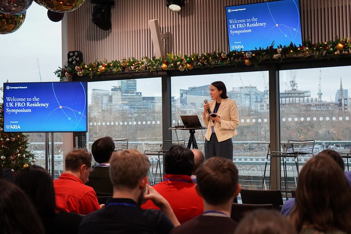 A women in a white blazer delivering a talk to a busy room (left hand side), A man presenting in a pink toned room (right hand side)