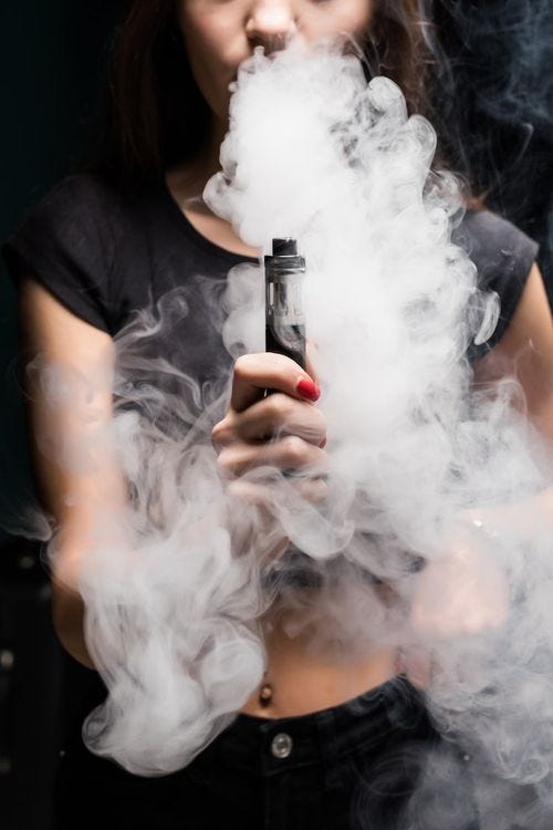 Free Photo young sexy woman is vaping smoking e-cigarette. cloud of vapor on the black wall