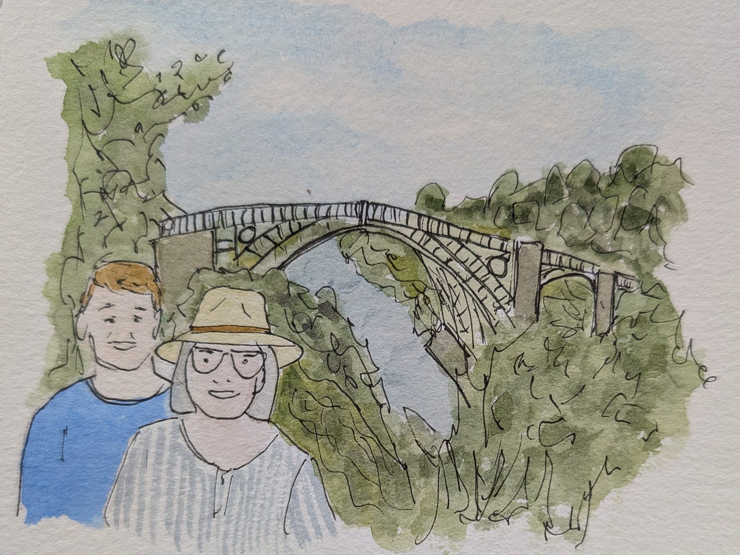 Loose ink and watercolour illustration of Andrea and Julian standing in front of the Iron Bridge at Ironbridge Gorge. Andrea is wearing a wide-brimmed cream hat and glasses, with Julian standing behind her. The historic iron arch bridge spans the wooded gorge in the background beneath a pale blue sky. Loose ink and watercolour illustration of Andrea and Julian standing in front of the Iron Bridge at Ironbridge Gorge. Andrea is wearing a wide-brimmed cream hat and glasses, with Julian standing behind her. The historic iron arch bridge spans the wooded gorge in the background beneath a pale blue sky.