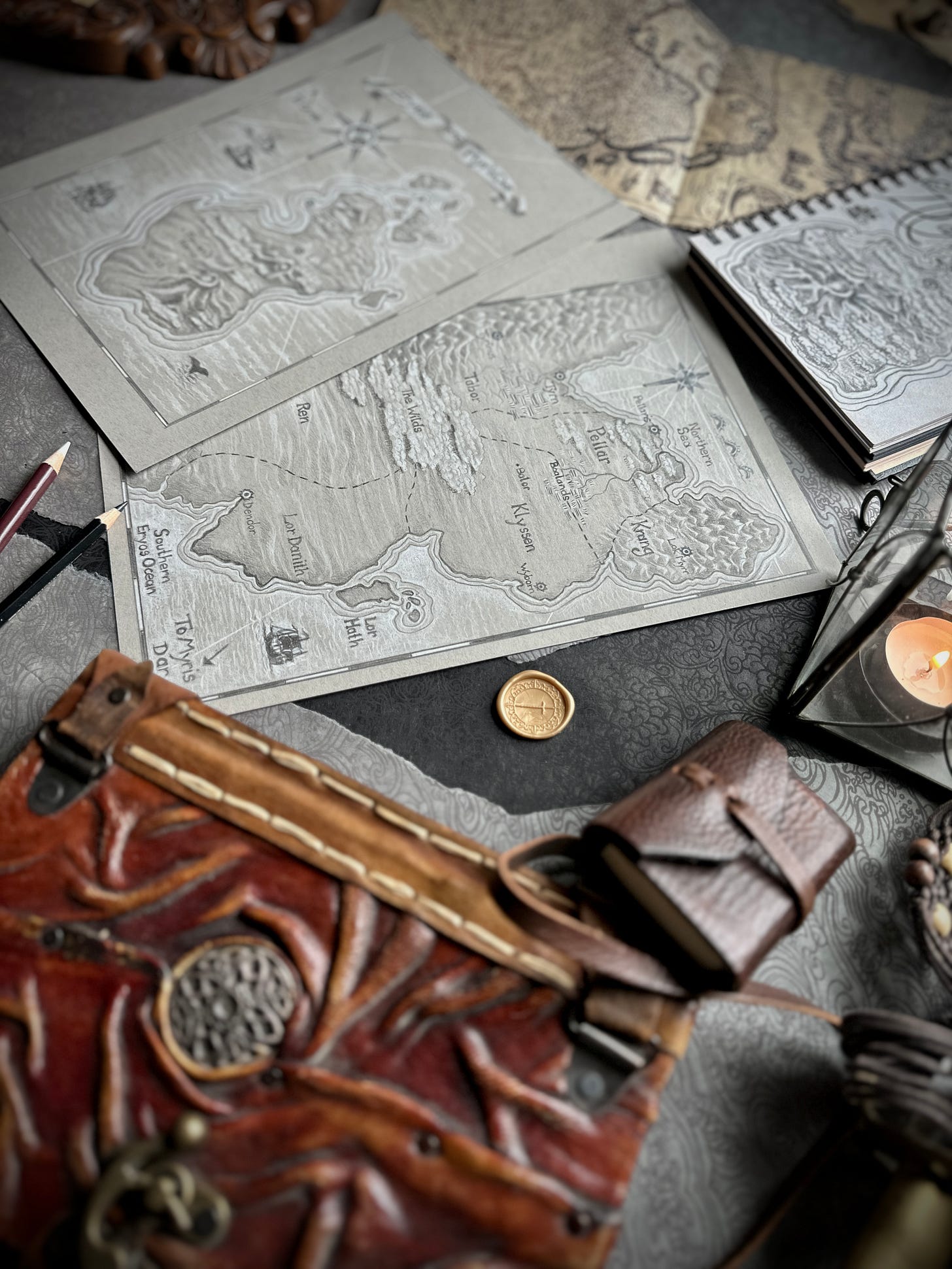 flat lay photo of the two new maps, an old leather book, a candle and pencils by Kindrie Grove