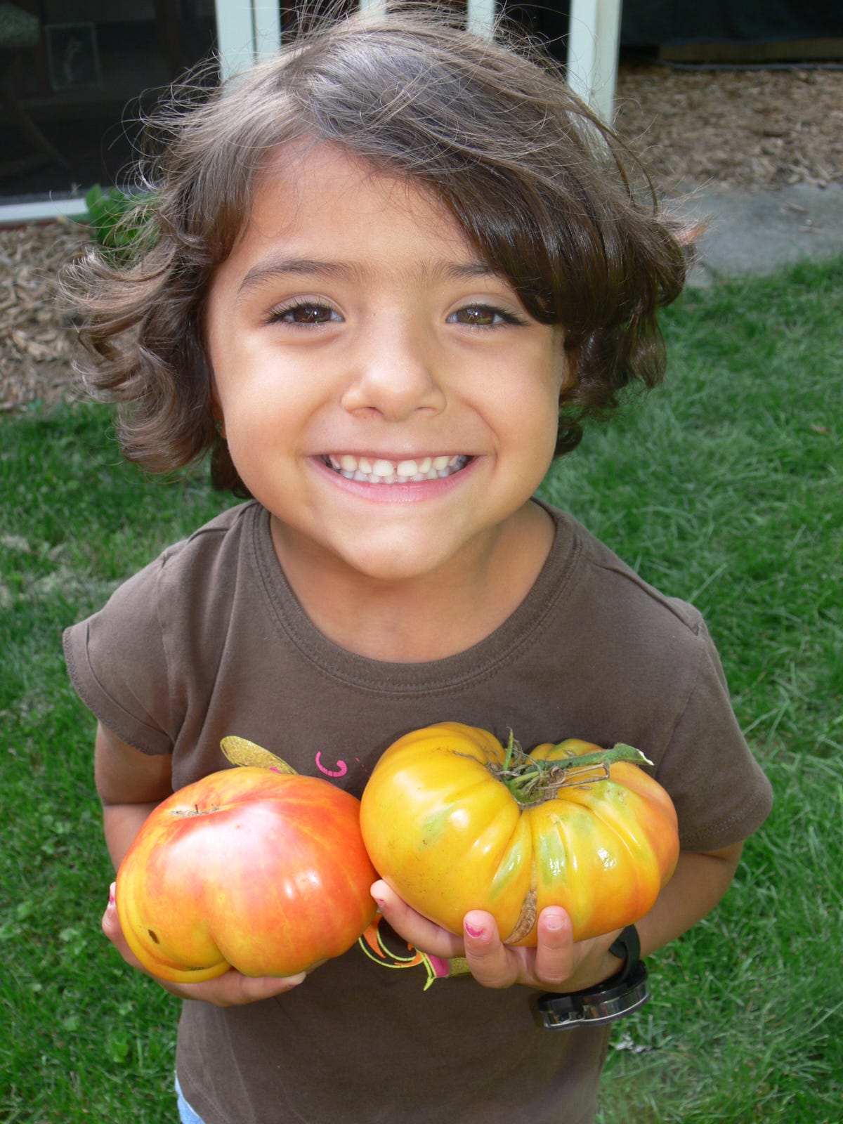 a young girl holding 2 heirloom tomatoes