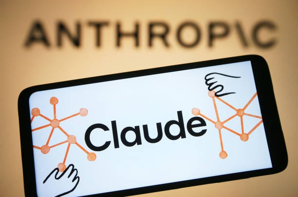 In this photo illustration, Claude AI logo is seen on a smartphone and Anthropic logo on a pc screen.