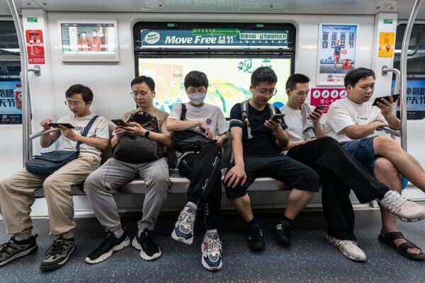 Men sitting in a subway car. most of them looking at their phones.
