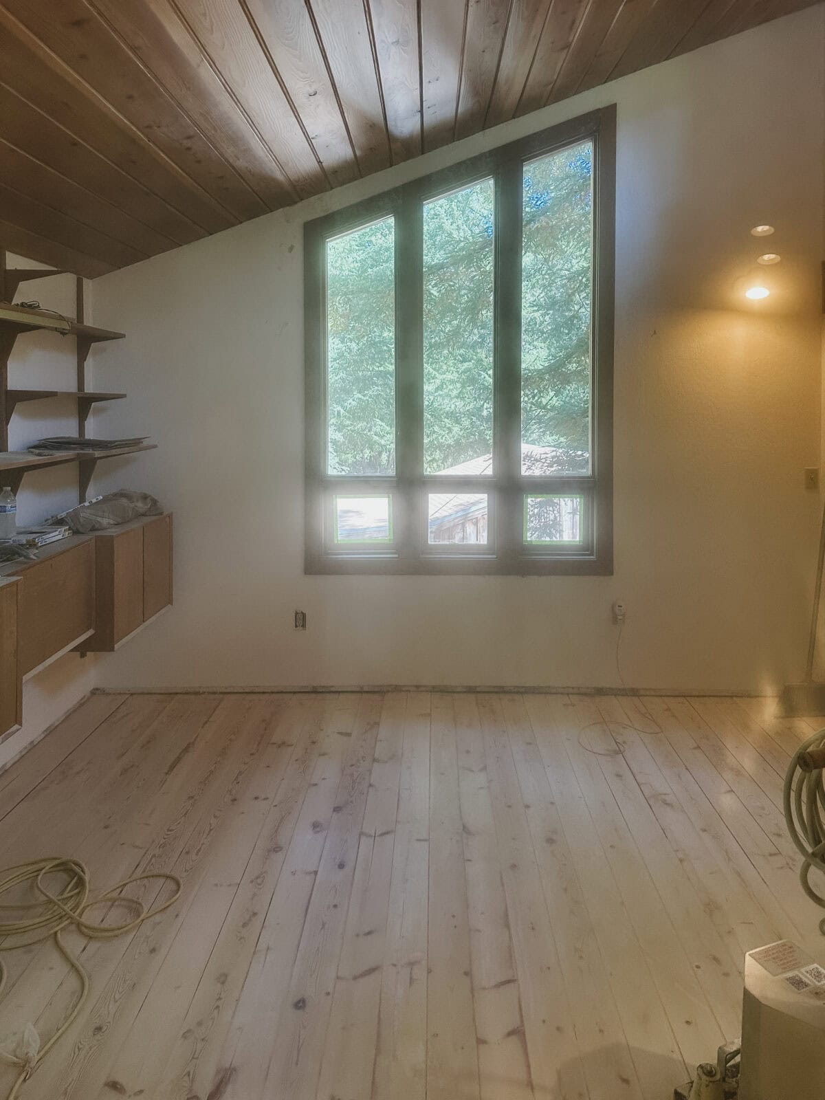 work in progress belt sander on pine floors with dust in the air looking out picture windows. 