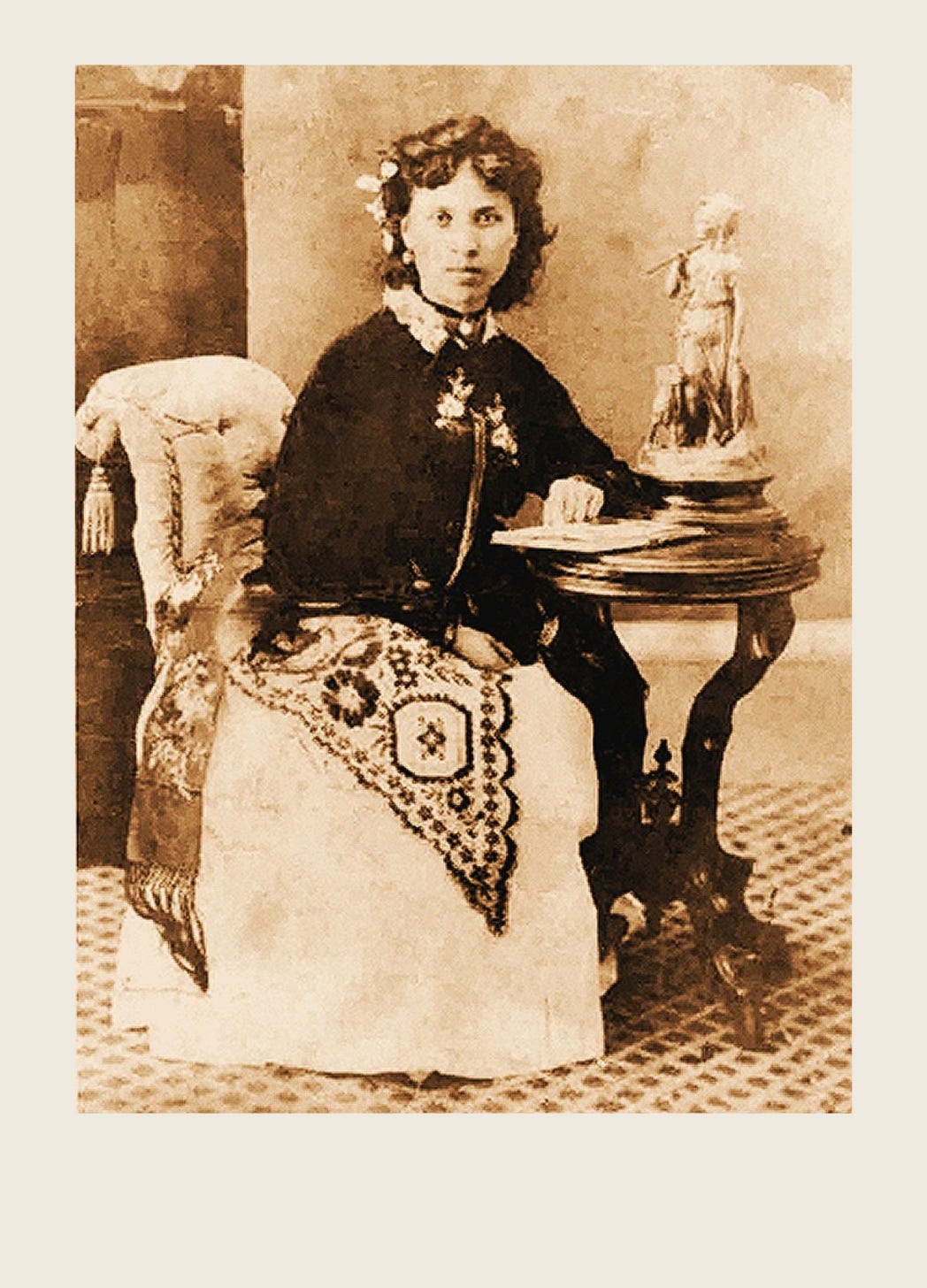 Portrait of a young Julia Yesler Benson Intermela seated beside a small table with a book and needlework, facing the camera.