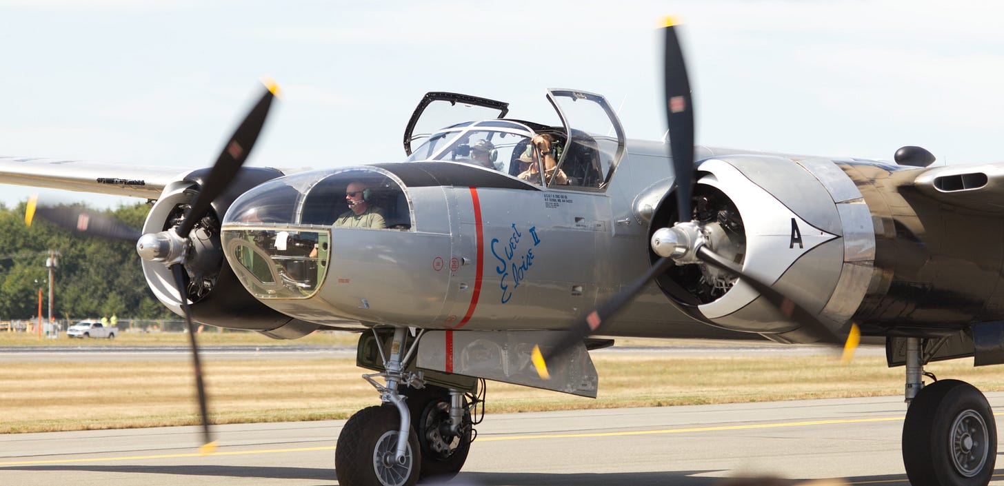 A dual-propeller plane taxing down a runway in bright sunlight.