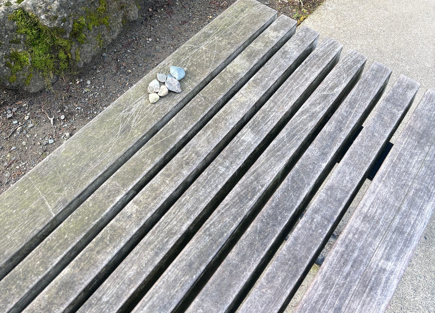Six small rocks on the edge of an empty wooden bench.