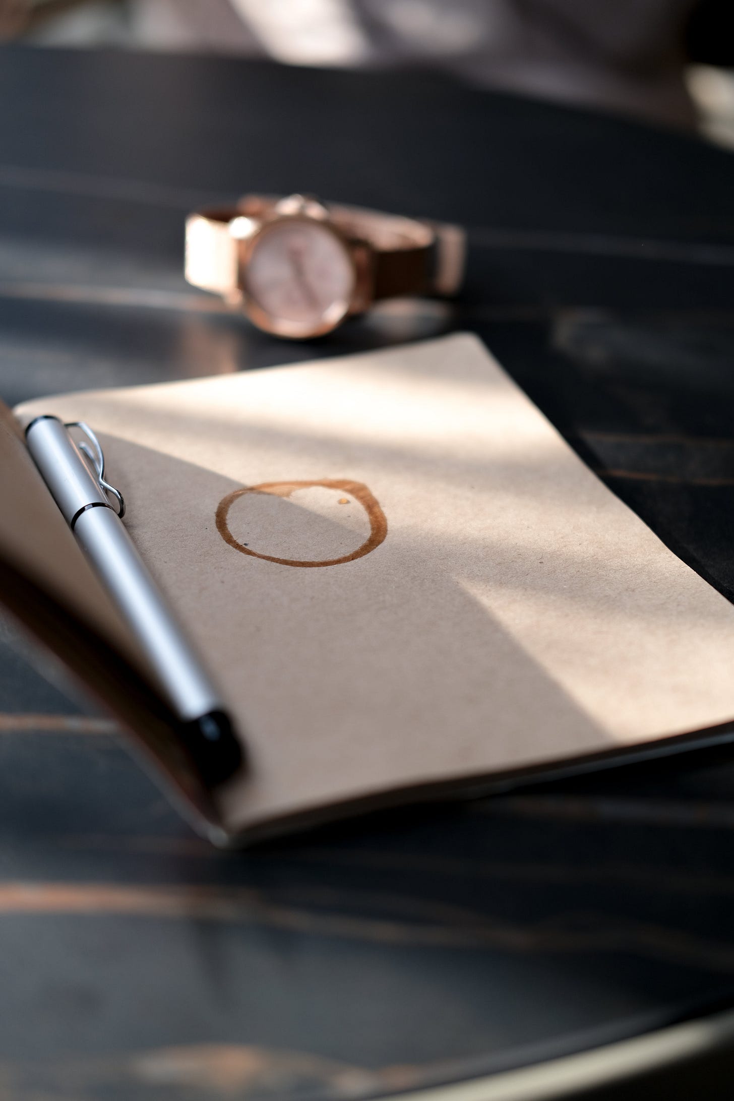 Notebook opened to coffee-stained page, a pen resting atop.