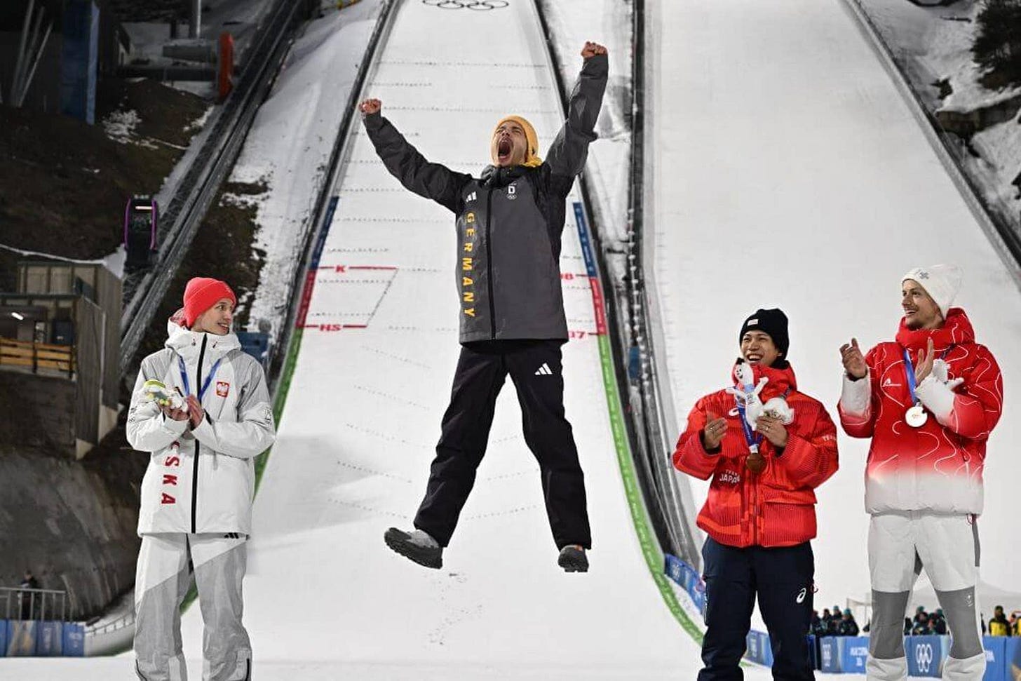 Philipp Raimund jumps for joy after winning gold in the men's normal hill ski jumping while the other medalists look on.