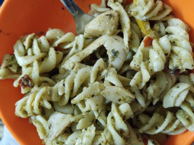 An orange bowl filled with fussili pasta with green sauce.