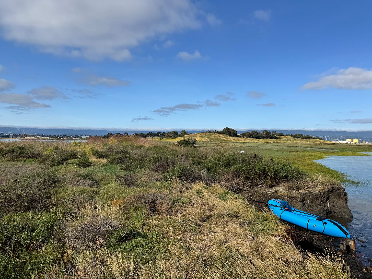 Packraft on shoreline of San Francisco Bay with office buildings on horizon