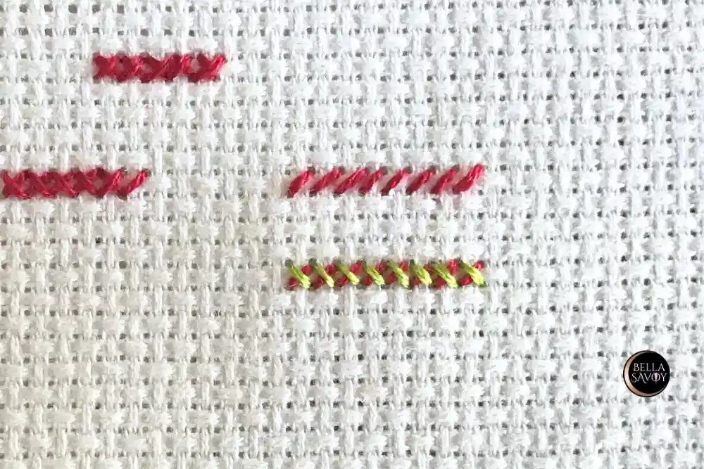 Close up of Aida fabric with one row of red half stitches and another row below to show the completed cross stitch using green thread.