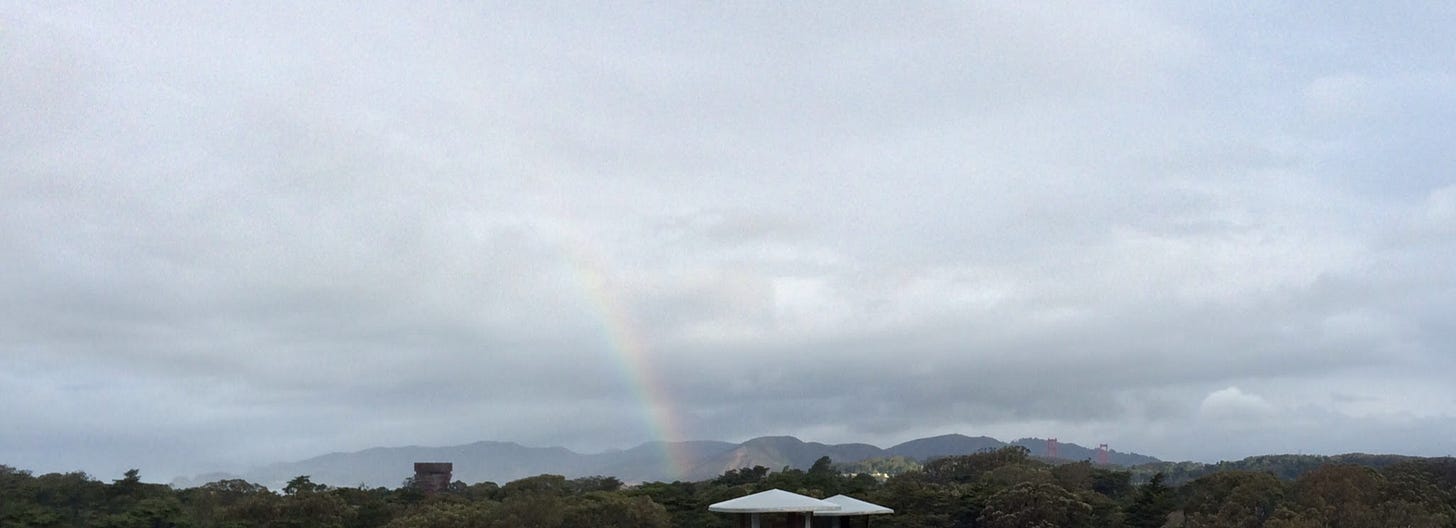 A light rainbow appears through the fog and clouds above the rooftops in San Francisco.