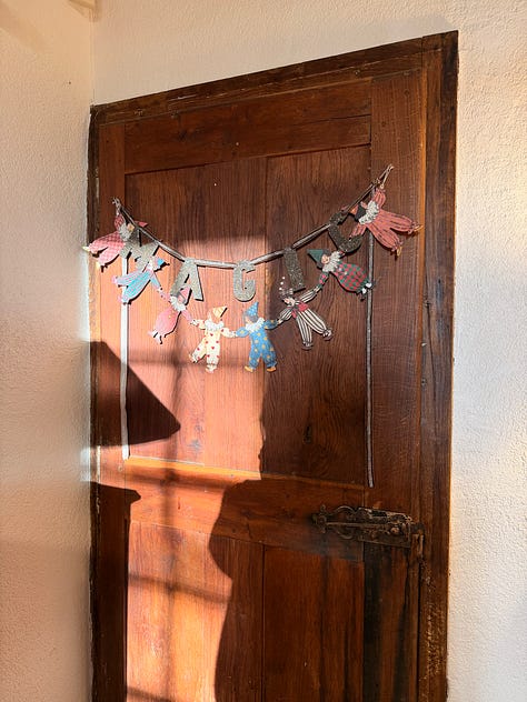Three doors at the château: an old dark wooden door hung with a paper fairy garland, a red painted door in a stone surround with a small girl reaching for the handle, and a large arched wooden double door where two children stand dressed as a fairy and a wizard.