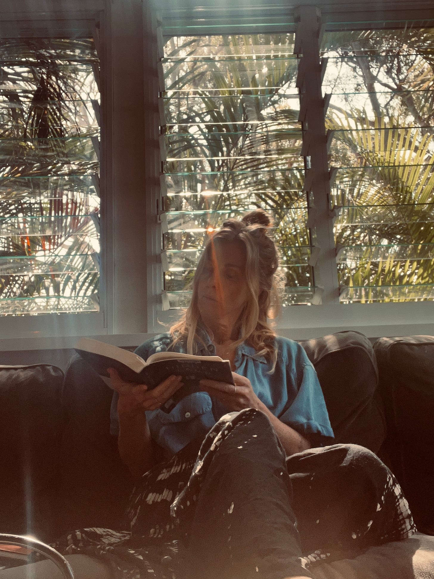 woman sitting by the window reading a book with light on her face